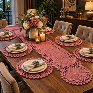 Puede incluir: Un camino de mesa de ganchillo en color rosa empolvado y manteles individuales circulares a juego sobre una mesa de comedor de madera. Cada mantel tiene un borde festoneado y sostiene un plato de cerámica blanca.