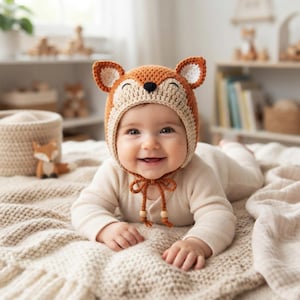 Può includere: Un cappello da volpe all'uncinetto in filato arancione e crema, con orecchie a punta dal centro bianco, un naso nero ricamato e occhi chiusi. Il cappello include lacci intrecciati con perline di legno alle estremità per legarlo sotto il mento.