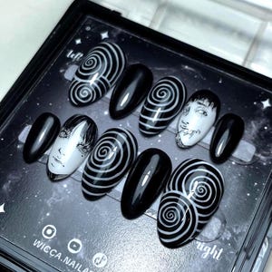 Puede incluir: Un juego de diez uñas postizas en blanco y negro. Los diseños incluyen uñas negras sólidas, uñas con patrones de espirales blancas y uñas con ilustraciones detalladas de rostros en blanco y negro. El conjunto se presenta en una caja.