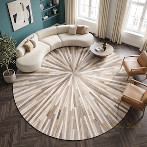 Può includere: Un grande tappeto circolare con un motivo a raggiera composto da strisce alternate di pelle o cuoio color beige chiaro, crema e marrone. Il tappeto è centrato in una stanza con un divano bianco curvo, due poltrone color cuoio e un tavolino rotondo.