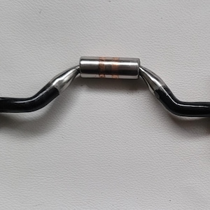 May include: A horse bit featuring two large circular stainless steel rings connected to a curved mouthpiece. The mouthpiece has black coated shanks on each side and a central cylindrical roller with a copper-colored band in the middle.
