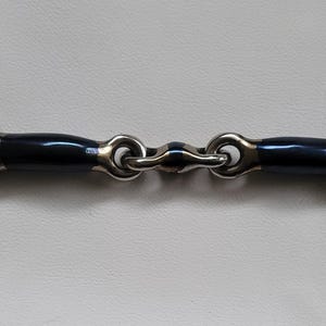 Könnte beinhalten: Ein Pferdegebiss mit zwei großen, runden Edelstahlringen, die mit einem zentralen Mundstück verbunden sind. Das Mundstück besteht aus zwei dunkelblauen, glatten, zylindrischen Segmenten, die durch ein kleines, zentrales Metallglied verbunden sind.