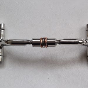 Op de afbeelding: Een zilverkleurig metalen paardenbit met twee grote cirkelvormige ringen aan de uiteinden en een centraal mondstuk. Het mondstuk bestaat uit twee gladde zilveren segmenten die in het midden verbonden zijn door twee kleine koperkleurige ringen.