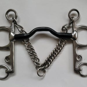 May include: A stainless steel horse bit featuring a black curved mouthpiece and a silver-coloured curb chain. The bit includes two side shanks with multiple rings for attachment, designed with a symmetrical structure and a central metal chain link.