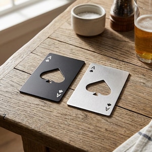 Può includere: Due apribottiglie rettangolari a forma di carte da gioco, uno nero opaco e uno argento spazzolato. Ognuno presenta un design ad asso di picche con un intaglio a forma di picche al centro e la lettera A con un piccolo simbolo negli angoli.