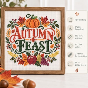 May include: A framed cross-stitch pattern featuring the text "AUTUMN FEAST" in red and green, surrounded by a wreath of pumpkins, leaves, apples, and grapes. The design includes 150 x 142 stitches, 17 DMC colours, and measures 27.20 x 25.76 cm.