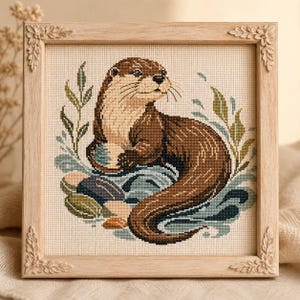 Peut inclure: Une broderie au point de croix représentant une loutre brune nageant dans l'eau avec du feuillage vert, encadrée dans un cadre en bois clair avec des sculptures de feuilles décoratives à chaque coin. La loutre est représentée de profil.