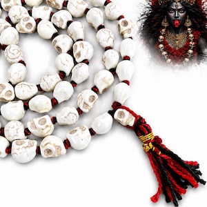 May include: A prayer bead necklace featuring white, skull-shaped beads with brown veining, strung on a red cord. The necklace ends in a red and black tassel with gold thread accents. An illustration of the Hindu goddess Kali is visible in the corner.