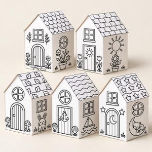May include: Five white cardboard house-shaped boxes with black line art illustrations for colouring. Each house features unique designs including flowers, a sun, a rabbit, a sailboat, and a cat on a crescent moon, with various roof patterns.