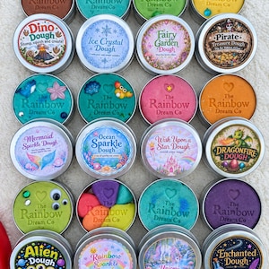 May include: A collection of twenty round metal tins filled with colourful modelling dough, each featuring a unique themed label such as Dino Dough, Ice Crystal Dough, Fairy Garden Dough, Pirate Treasure Dough, Mermaid Sparkle Dough, and others.