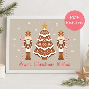 Può includere: Uno schema a punto croce con un albero di Natale centrale in stile pan di zenzero affiancato da due schiaccianoci con bastoncini di zucchero, su sfondo beige con fiocchi di neve bianchi e il testo Sweet Christmas Wishes in rosa.