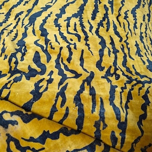 May include: A piece of fabric featuring a bold tiger stripe pattern in deep black against a vibrant mustard yellow background. The material has a soft, slightly textured surface with visible folds and a raw, unfinished edge at the top.
