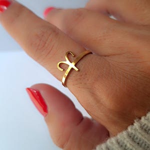 May include: A gold-toned ring featuring a stylised Aries zodiac symbol as the centrepiece. The band is thin and circular, with the ram horn motif extending upwards from the top of the band. The metal has a smooth, polished finish throughout.