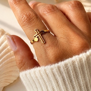 Peut inclure: Une bague dorée présentant un motif de croix découpé centré sur un anneau fin et poli. La bague possède une finition métallique lisse et réfléchissante ainsi qu'une structure ouverte permettant un ajustement confortable sur le doigt.