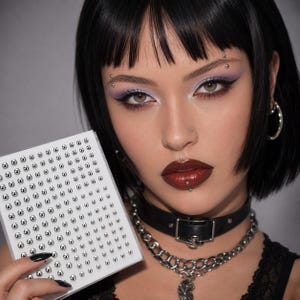 May include: A square sheet of small, metallic silver adhesive face gems arranged in a grid pattern. The individual circular studs have a polished, reflective finish and are designed for decorative application on the skin or other surfaces.