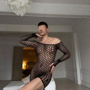 Könnte beinhalten: Ein schwarzes Netz-Minikleid mit weitem, schulterfreiem Ausschnitt und langen Ärmeln. Das Kleidungsstück besteht aus einem kreisförmigen Netzmuster, das einen halbtransparenten Effekt über das gesamte Teil erzeugt und am Oberschenkel endet.
