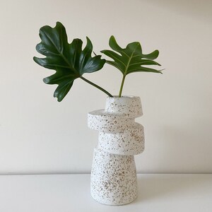 A-symmetrical vase in offwhite with brown speckles. This unique interior accessory is handmade from a mould. The mould is made from a unique vase I made on a potterswheel. This shape is perfect match to a Scandinavian and Japandi style interior.