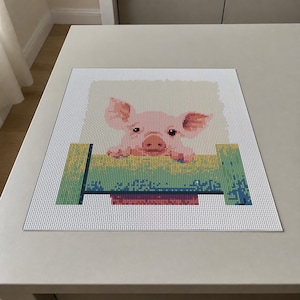 May include: A square diamond painting craft project featuring a pixelated image of a pink piglet resting its front hooves on a green fence. The design is set against a white background with a grid of circular adhesive dots for applying beads.