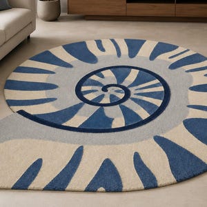 May include: A large, round area rug featuring a stylized nautilus shell design. The rug displays a repeating pattern of deep blue, light blue, and cream-colored segments that spiral outward from the center, creating a distinct shell-like shape.