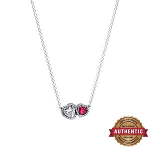 May include: A silver chain necklace featuring a pendant with two heart-shaped stones, one clear and one red, surrounded by small clear crystals. The pendant is attached to a delicate silver link chain that hangs in a V-shape against a white background.