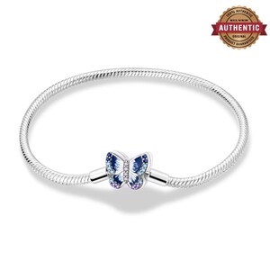 Può includere: Un bracciale a catena snake in argento con una chiusura a forma di farfalla. La farfalla è decorata con smalto blu e bianco, piccole pietre trasparenti al centro e minuscole pietre viola sui bordi inferiori delle ali.