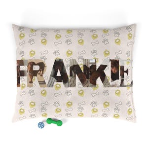 May include: A rectangular throw pillow with a light beige background featuring a repeating pattern of yellow dog bandanas, white bones, and gray paw prints. The name FRANKIE is printed in large letters filled with photos of dachshunds.