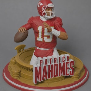 May include: A Patrick Mahomes figurine wearing a red Kansas City Chiefs jersey with the number 15, a red helmet, and white pants. The figure is in a throwing pose holding a brown football, set atop a circular stadium base with the name Patrick Mahomes.