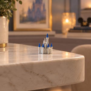 May include: A miniature white castle figurine featuring multiple towers with pointed blue roofs. The structure has a central main tower surrounded by smaller turrets, all rendered in a solid, matte finish with detailed architectural elements.