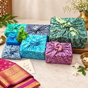 Pode incluir: Uma coleção de caixas de presente quadradas embrulhadas em tecido estampado colorido usando o método furoshiki, com nós no topo em tons de azul, verde e roxo, acompanhadas por um cartão branco com o texto A Special Gift e um coração.