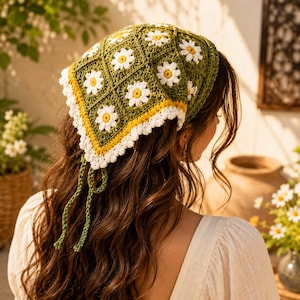 May include: A triangular crochet headscarf featuring a repeating pattern of white daisy motifs with yellow centers on a dark olive green background, finished with a bright yellow border and a white scalloped edge, including two long green ties.