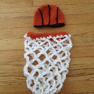 May include: A white crocheted basketball hoop with an orange and black crocheted basketball on top.