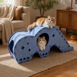 Puede incluir: Un túnel y estructura de escalada para gatos de fieltro azul claro con un diseño arqueado de varios niveles, con recortes circulares y en forma de estrella, ensamblado con costuras azules visibles, ocupado por dos gatos de pelo largo.