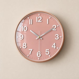 May include: A round wall clock featuring a metallic copper-toned frame and a solid dusty pink face. The clock displays large, raised white Arabic numerals for the hours, complemented by slender silver-colored hour, minute, and second hands.