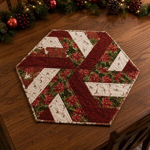May include: A hexagonal quilted table mat featuring a pinwheel pattern. The fabric displays a festive design with deep red poinsettias, green holly leaves, and cream-colored sections decorated with small sprigs of holly berries and leaves.
