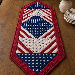 May include: A quilted table runner featuring a patriotic design with red, white, and blue colors. The runner displays geometric patterns of stars on blue backgrounds, white fabric with small red and blue stars, and diagonal red and white stripes.