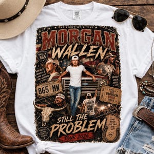 Puede incluir: Una camiseta blanca con un estampado gráfico del cantante de country Morgan Wallen. El diseño incluye varias imágenes del artista, un camión, un cráneo de buey y el texto Morgan Wallen, Still The Problem Tour 2026 y 865 MW.