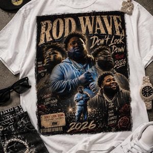 May include: A white t-shirt featuring a graphic print of Rod Wave with the text "Rod Wave," "Don't Look Down Tour 2026," "Pain Made Me Music Saved Me," "Heart Over Everything," "Love Pain Loyalty Legacy," and "2026" in a distressed, concert-poster style.