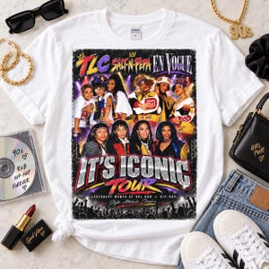 Pode incluir: Uma t-shirt branca de gola redonda com uma impressão gráfica da digressão musical dos anos 90 intitulada It's Iconic Tour, exibindo imagens dos grupos musicais TLC, Salt-N-Pepa e En Vogue com texto colorido e uma silhueta de público abaixo.