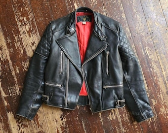 May include: A black leather motorcycle jacket featuring a vibrant red quilted lining, silver-tone metal zippers, a notched collar, and quilted shoulder panels. The jacket includes two zippered chest pockets, two lower zippered pockets, and adjustable side buckles.