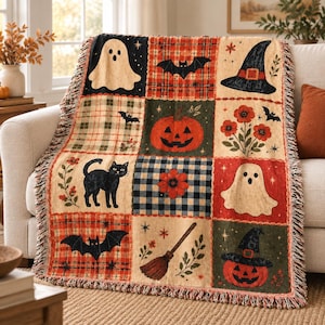 May include: A woven throw blanket featuring a grid of nine squares with Halloween motifs including ghosts, jack-o'-lanterns, black cats, bats, a witch's hat, a broom, and floral patterns in orange, black, cream, and green with fringed edges.