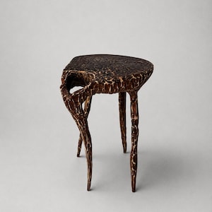 Puede incluir: Un taburete de madera marrón oscuro con una superficie tallada y texturizada. El taburete presenta una parte superior redonda y tres patas delgadas e irregulares. La madera muestra un acabado profundo y moteado con marcas de gubia visibles en toda la estructura, creando una apariencia robusta y orgánica.