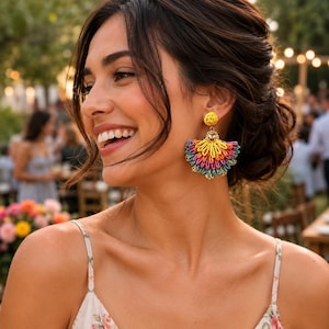 May include: A pair of fan-shaped drop earrings featuring a vibrant, multi-colored woven thread design in shades of yellow, orange, pink, and teal. The earrings are anchored by a small, circular yellow stud at the top, creating a layered, textured look.