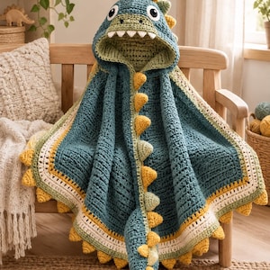 May include: A teal crochet hooded blanket featuring a dinosaur design with a hood that has eyes, white teeth, and yellow spikes. The blanket has a long tail with yellow spikes and a border with alternating stripes of cream, yellow, and light green.