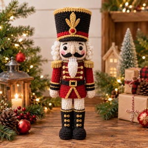Puede incluir: Una muñeca cascanueces tejida a ganchillo con un sombrero negro alto con un emblema dorado, una chaqueta roja con adornos y botones dorados, pantalones blancos y botas negras. La figura tiene barba blanca, bigote negro y mejillas rosadas.