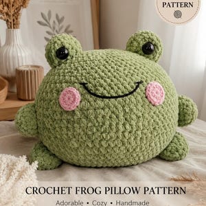May include: A round, green crochet frog pillow with two protruding eyes, black plastic pupils, and two pink circular cheeks. The frog has a stitched black mouth. The text reads PDF PATTERN and CROCHET FROG PILLOW PATTERN Adorable Cozy Handmade.