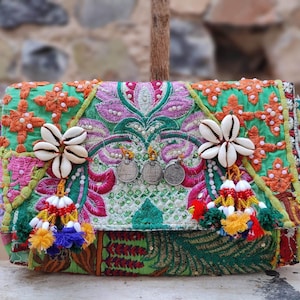 May include: A rectangular clutch bag featuring vibrant green fabric with intricate multi-coloured embroidery, floral patterns, and small sequins. The front is decorated with two white cowrie shell clusters, three hanging silver-toned coins, and colourful tassels.