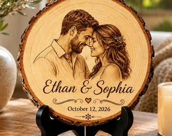 May include: A circular wood slice plaque featuring a laser-engraved portrait of a couple facing each other. The text reads Ethan & Sophia with the date October 12, 2026, below a small heart icon. The plaque rests on a black plastic display stand.