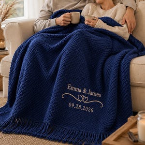 May include: A deep navy blue textured knit throw blanket featuring fringe trim along the bottom edge. The blanket is embroidered with the text Emma & James, two interlocking heart icons, and the date 09.28.2026 in a light beige thread.