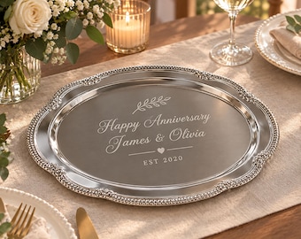 May include: An oval silver-toned serving tray with a decorative beaded and floral embossed rim. The center is engraved with a leaf sprig, the text "Happy Anniversary James & Olivia", a small heart icon, and the text "EST 2020" in a clean font.