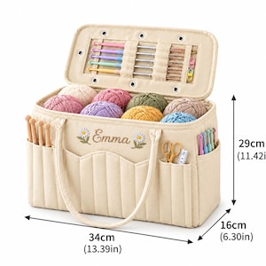 May include: A beige fabric yarn storage bag with the name Emma embroidered between two daisy flowers. It features multiple pockets, internal crochet hook loops, and yarn balls. Dimensions are 34cm (13.39in) wide, 16cm (6.30in) deep, and 29cm (11.42in) high.